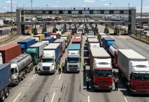 Role of China in Mexico Supply Chains Evaluated by USMCA Line of semi-trucks queued at a toll plaza under an overhead gantry, with workers guiding traffic in high-visibility vests.