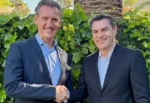 Noatum Logistics Has Acquired Germany-Based MBS Logistics Two men in dark suits shake hands and smile outdoors in front of a green hedge.