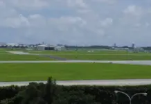 Amentum to Modernize Defense Supply Chain With $77m Deal Wide view of an airport with green grass fields, hangars, and a distant control tower under a cloudy sky.