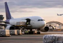FedEx Non-Stop Freighter Service Boosts Intra-Asia Network Cargo jet on the tarmac unloading palletized cargo with ground crew nearby; control tower and a city skyline in the background.