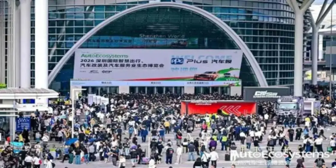 Crowd of people gathered outside a large modern convention center with a glass arch and banners advertising the expo, indicating a busy conference scene.